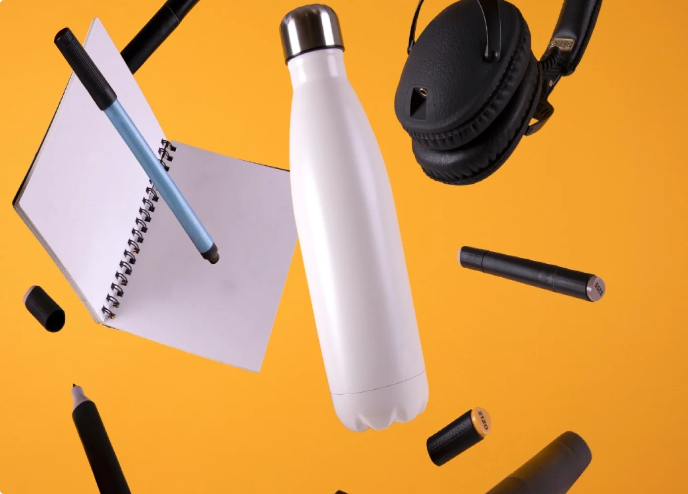 Eine weiße Wasserflasche, umgeben von Kugelschreibern, Bleistiften und einem Notizbuch
