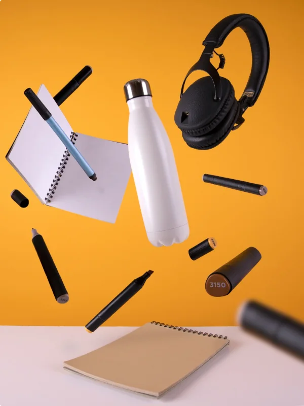 Eine weiße Wasserflasche, umgeben von Kugelschreibern, Bleistiften und einem Notizbuch