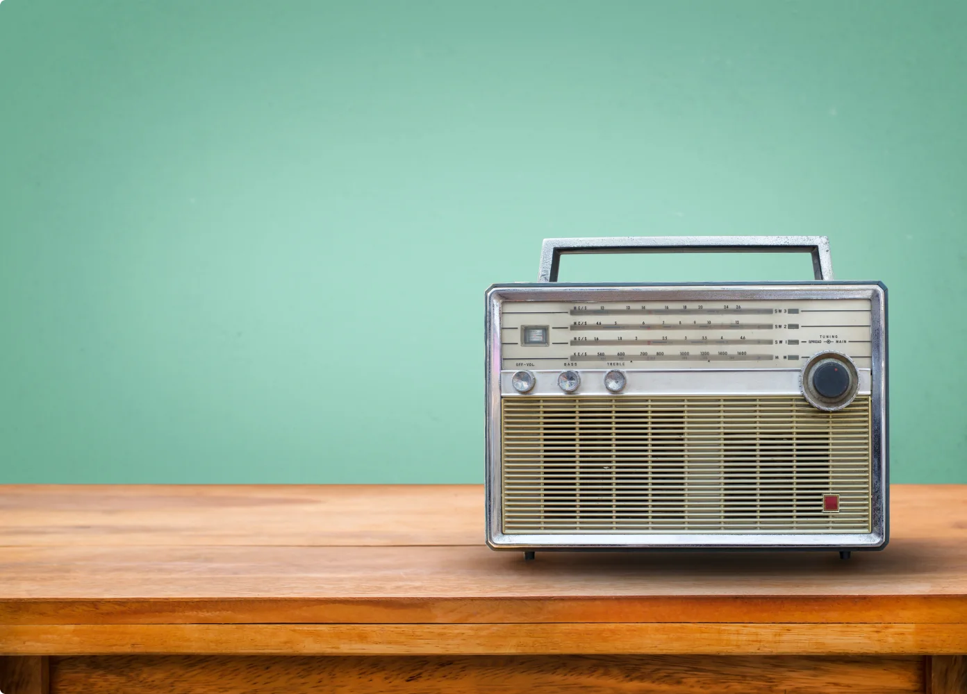Ein altes Radio auf einem Holztisch vor einer grünen Wand.