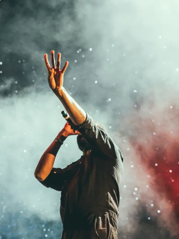 Ein Sänger auf der Bühne mit erhobenen Händen bei einem Konzert.