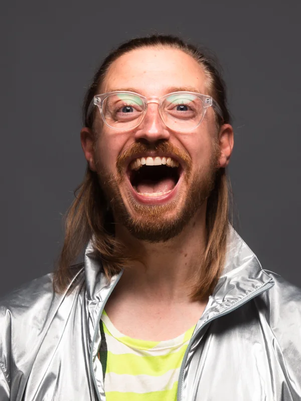Ein Moderator mit Brille in einer silbernen Jacke und weit geöffneten Mund beim Lachen