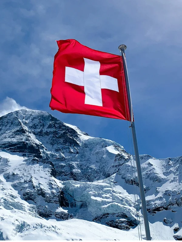 Schweizer Flagge weht vor schneebedecktem Berg und blauem Himmel