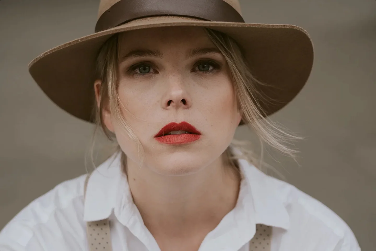 Eine Musicaldarstellerin in einem weißen Hemd, mit braunem Hut und rotem Lippenstift blickt direkt in die Kamera.