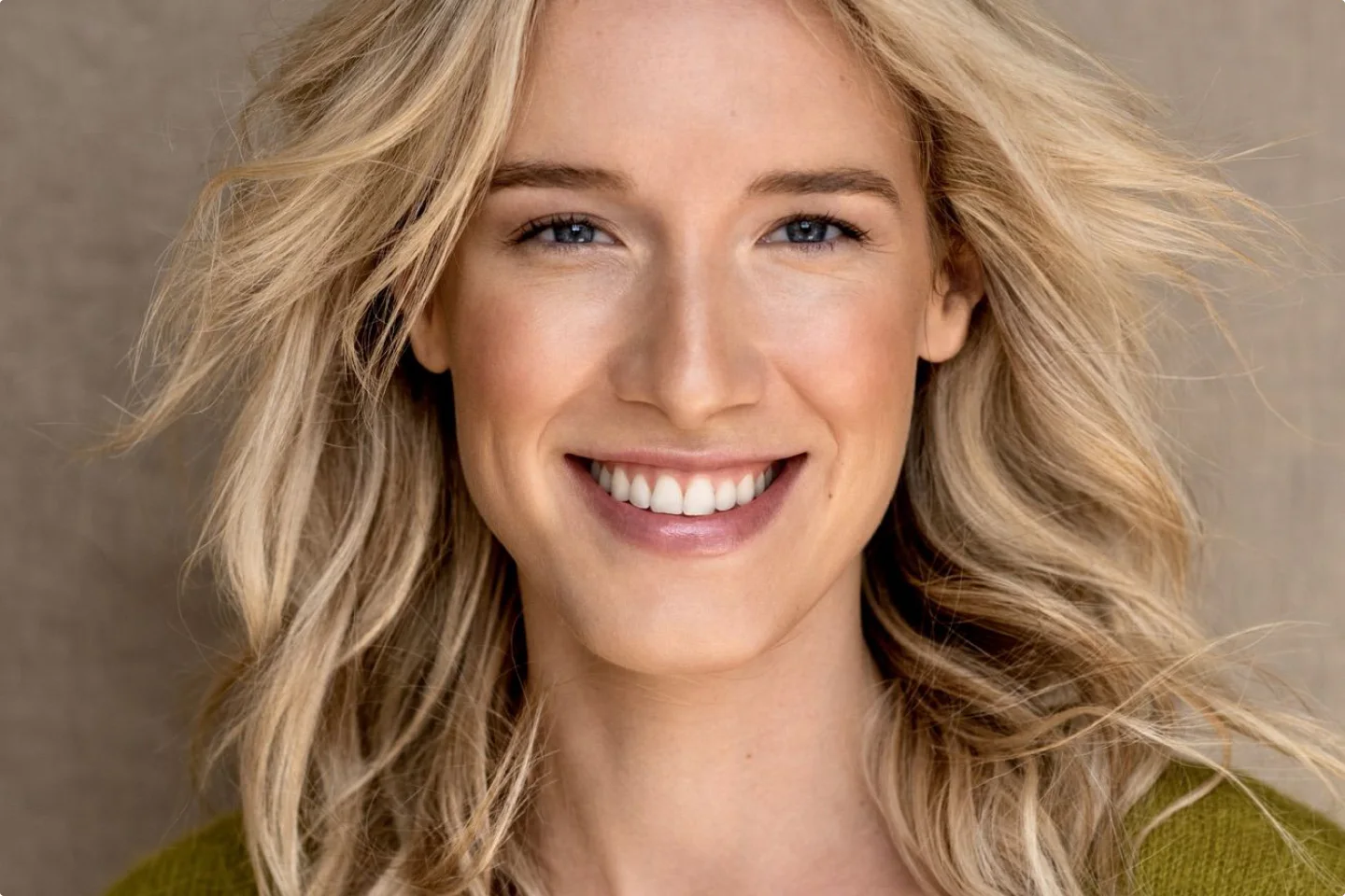Eine blonde Moderatorin mit lockigem Haar lächelt in die Kamera