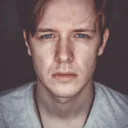 Ein junger Mann mit ernstem Gesichtsausdruck schaut direkt in die Kamera