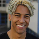 Lächelnder Mann mit blondierten Dreadlocks trägt ein schwarzes Oberteil