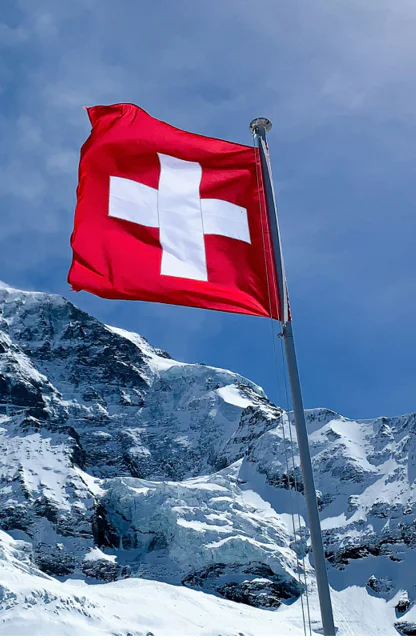 Schweizer Flagge weht vor schneebedecktem Berg und blauem Himmel